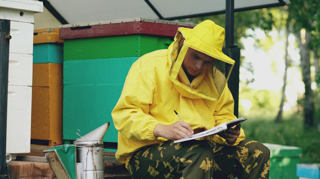 Hands writing notes in a notebook next to a laptop on a wooden desk